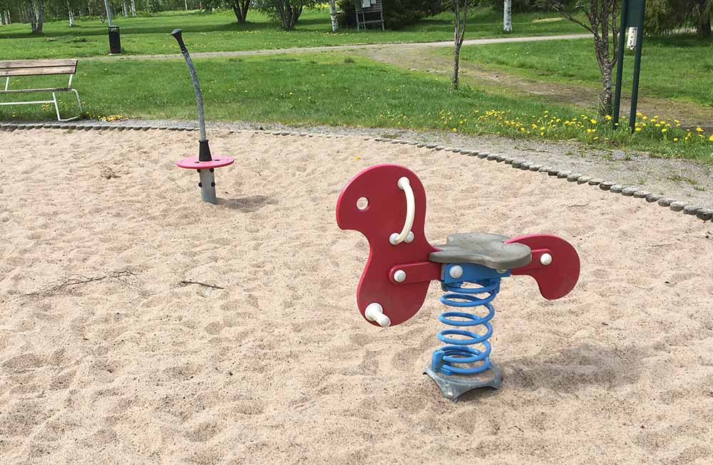 Gungleksak i form av en röd häst, står i sand.