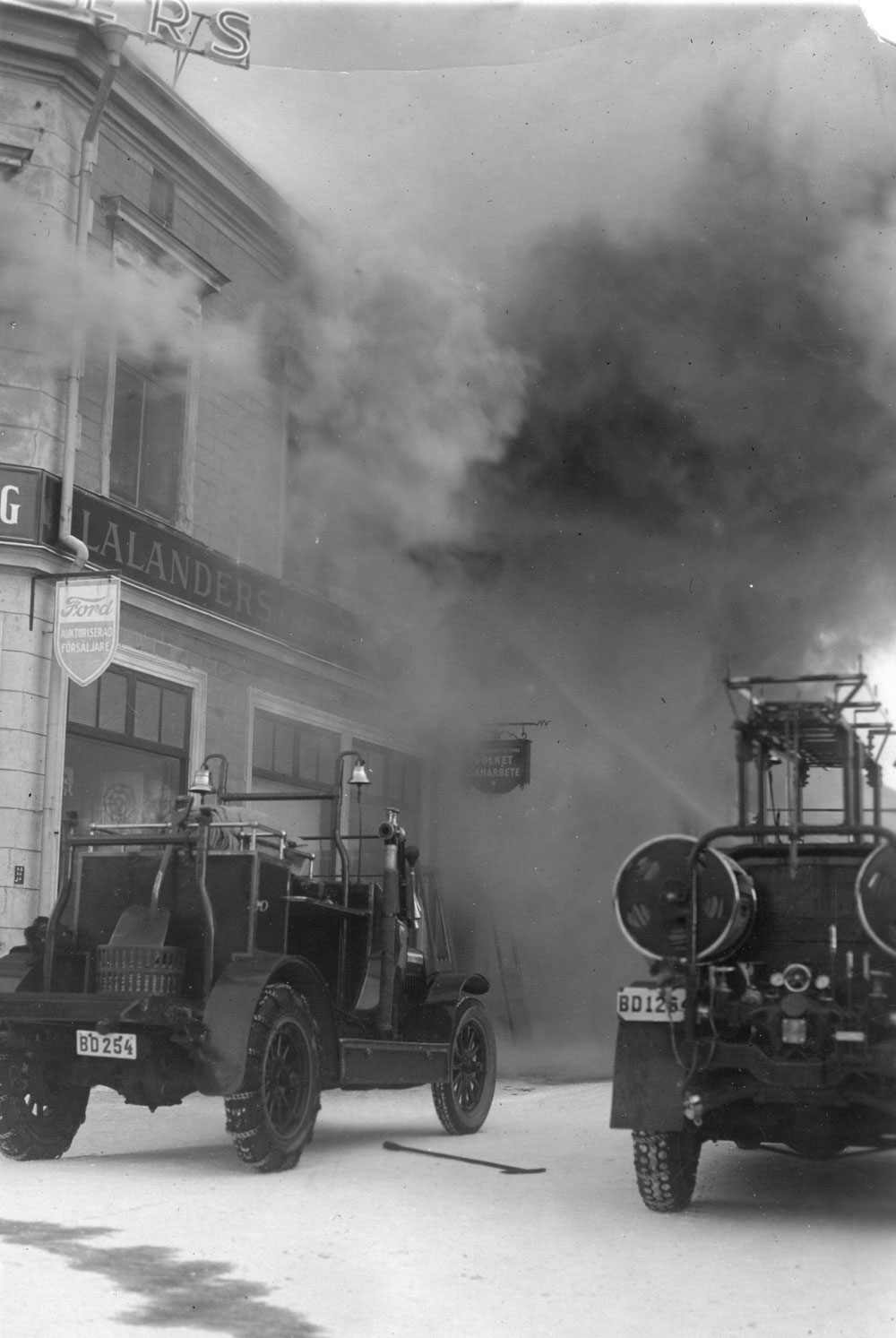 Rök väller ut från hus, på gatan står två brandbilar.