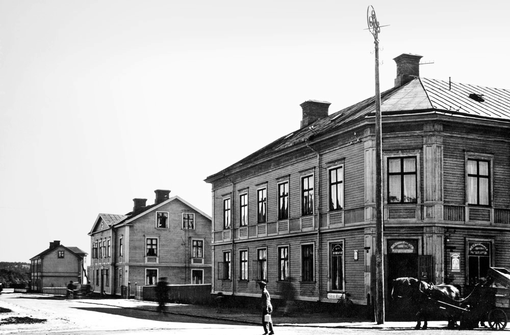 Trähus vid stadsgata. Häst och vagn i vägkorsningen.