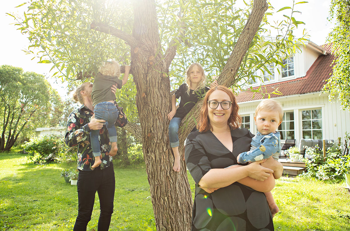 En familj med en mamma, en pappa och tre barn som står framför ett träd i en villaträdgård